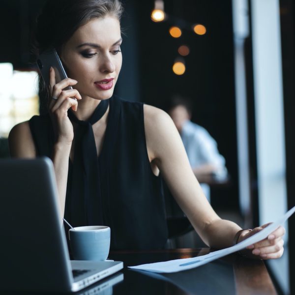 Young charming woman calling with cell telephone while sitting in coffee shop during free time, attractive female having talking conversation with mobile phone while rest in cafe